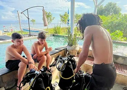 Two children watching a diving instructor prepare scuba gear at Bali Center Dive.