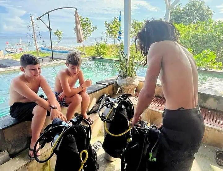 Two children watching a diving instructor prepare scuba gear at Bali Center Dive.